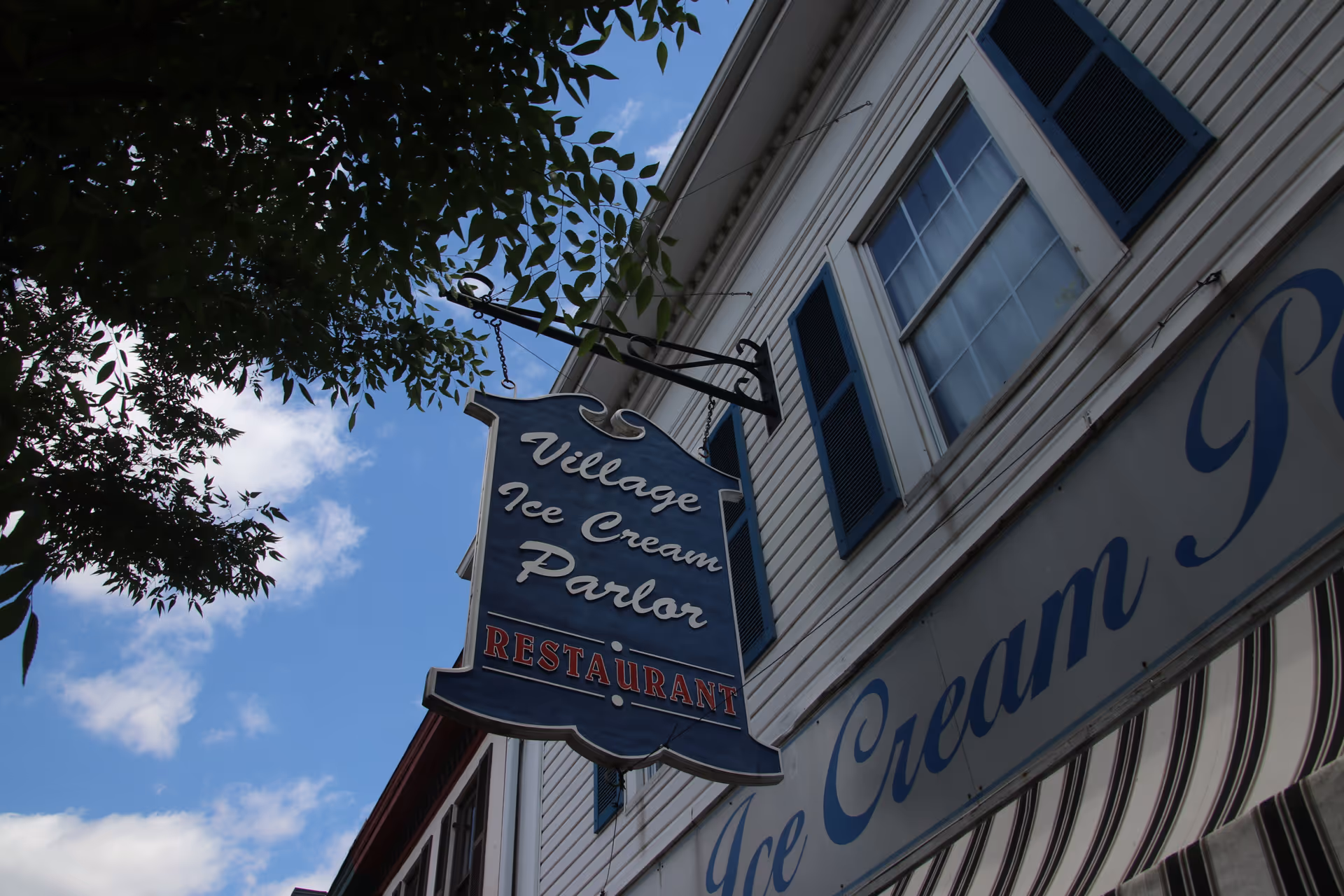 Exterior view of a blue Village Ice Cream Parlor sign on a white building.