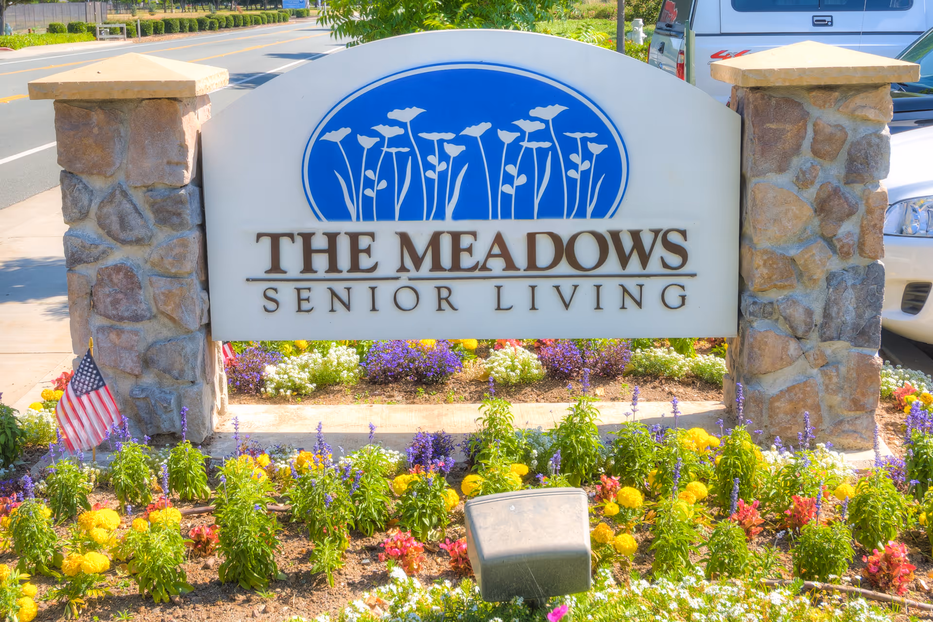Stone-framed sign reading The Meadows Senior Living with colorful flowers in front.