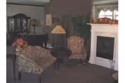 Cozy resident living room with upholstered chairs, a sofa, lamp, fireplace, and potted plants.