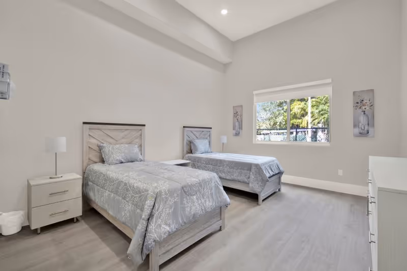 Two twin beds with matching gray bedding and nightstands in a bright, minimalist bedroom.