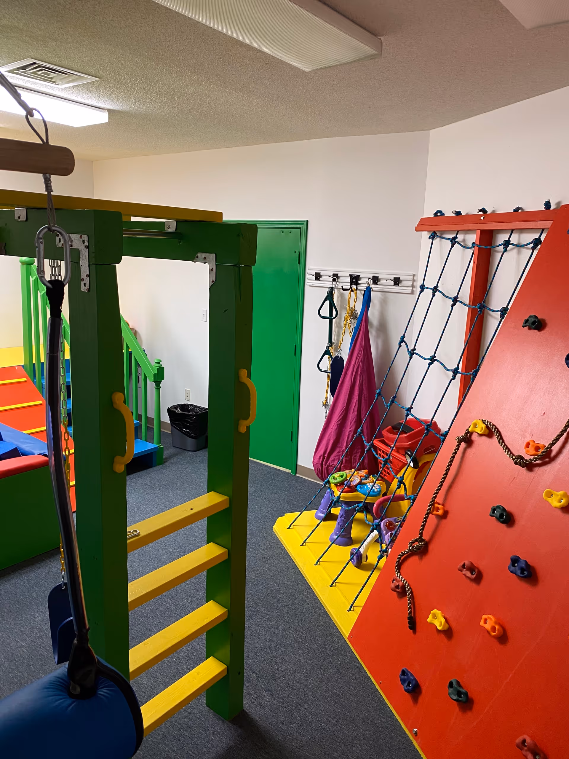 Colorful indoor therapy room with climbing wall, ropes, and fitness equipment.