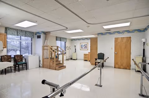 Interior rehabilitation area in a senior facility with parallel bars and seating.