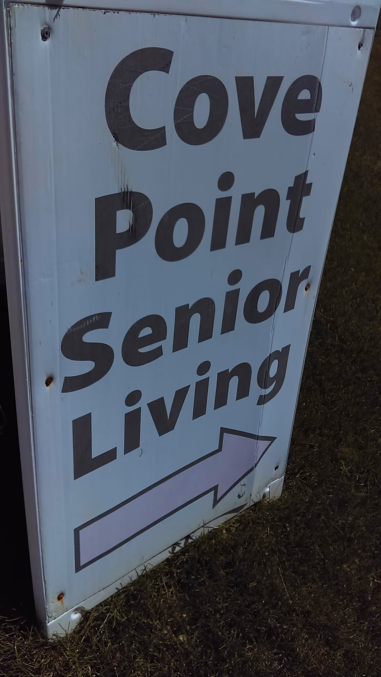 Exterior sign reading Cove Point Senior Living with a purple arrow on grass