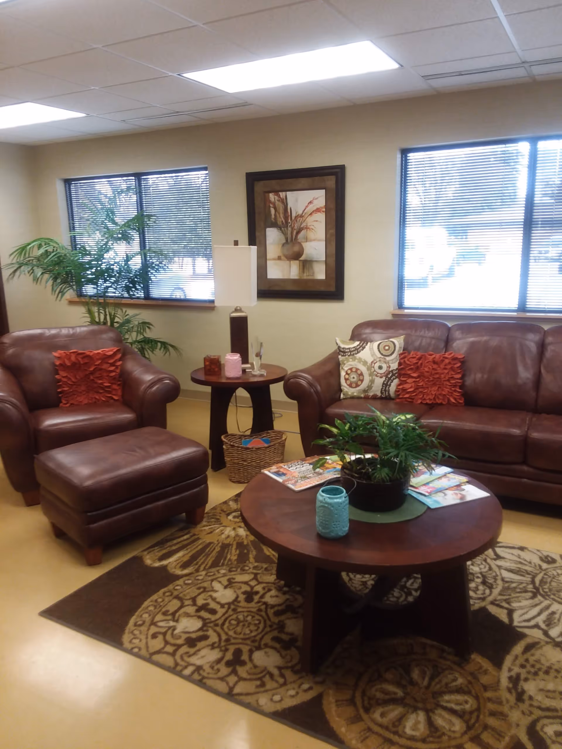A cozy lounge area with brown leather sofas, tables, plants, and decorative cushions.