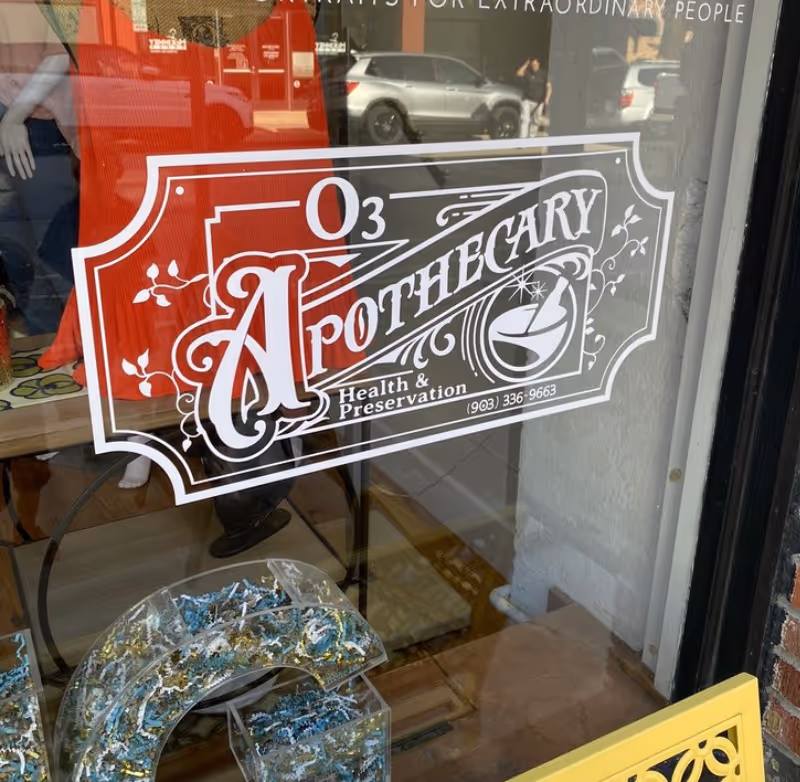 Storefront window with O3 Apothecary logo and reflections of cars.