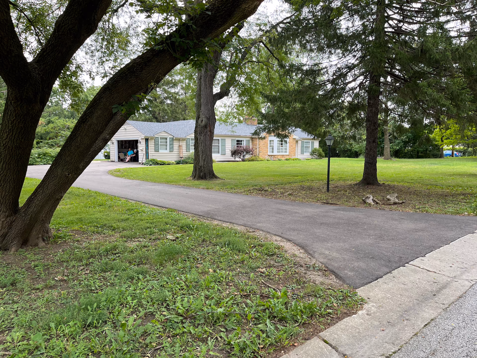 Single-story residential-style senior facility exterior with a curved driveway, green lawn, and trees.
