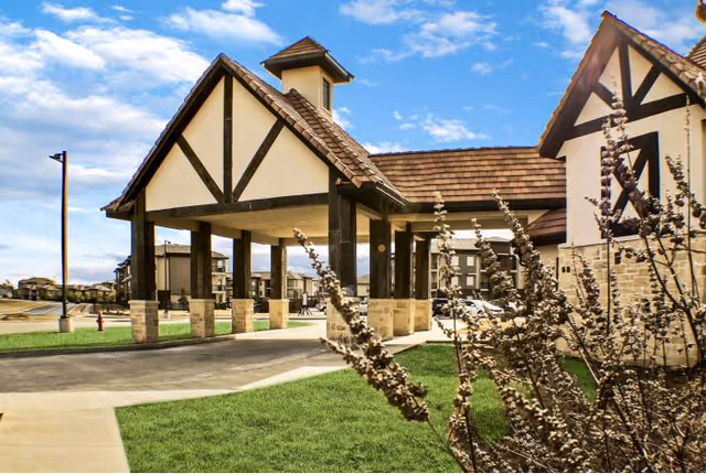 Exterior view of The Highlands At Owasso entrance with a covered porte-cochère and landscaping.