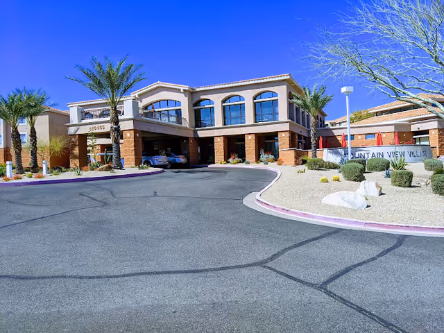 Exterior view of Fountain View Village senior living facility with palm trees and a curved driveway.