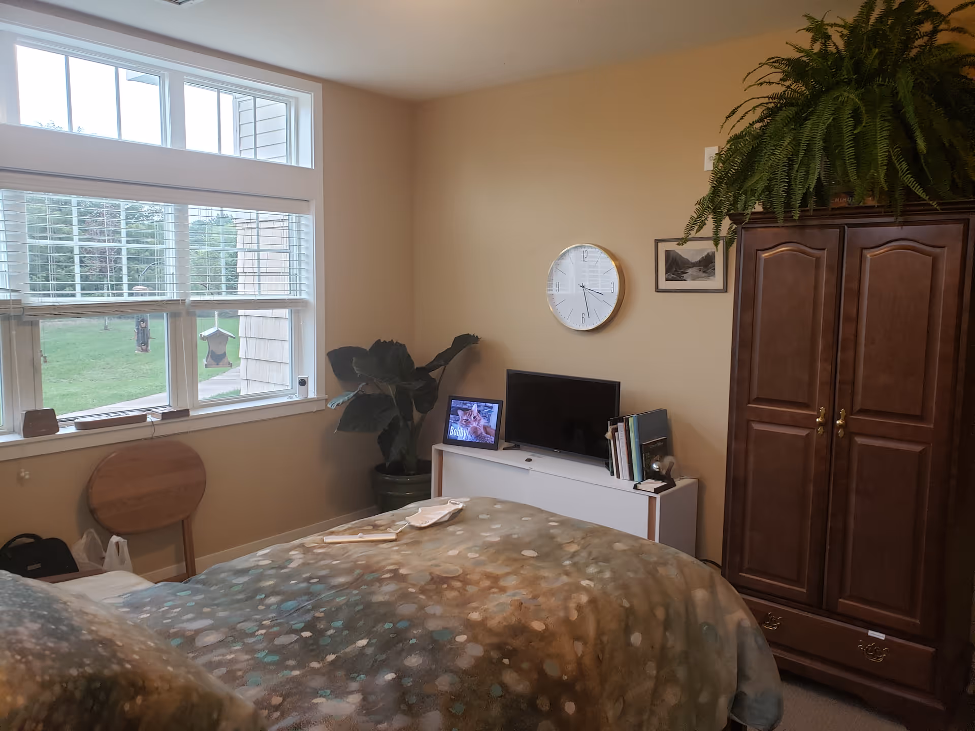 Bedroom in Stoney River Ramsey featuring bed, dresser, armoire, plants, window, clock, and TV.