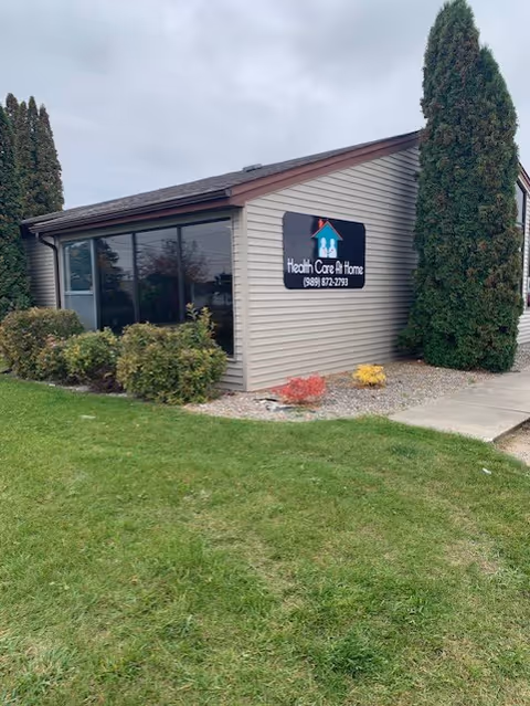 Exterior view of Health Care At Home building with sign, landscaping, and sidewalk.