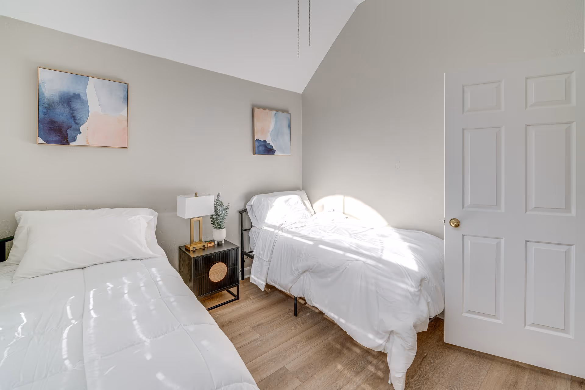 Two twin beds in a bright neutral bedroom with a nightstand.