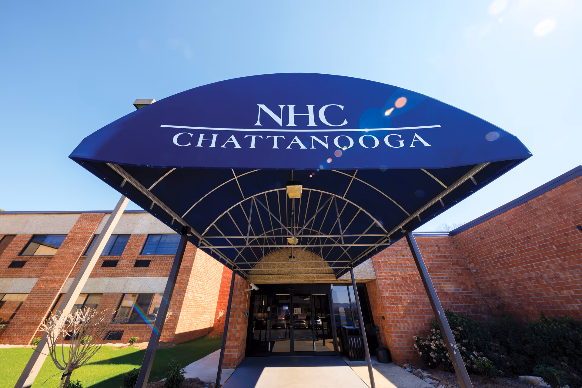 Blue curved canopy with NHC Chattanooga sign over brick building entrance.