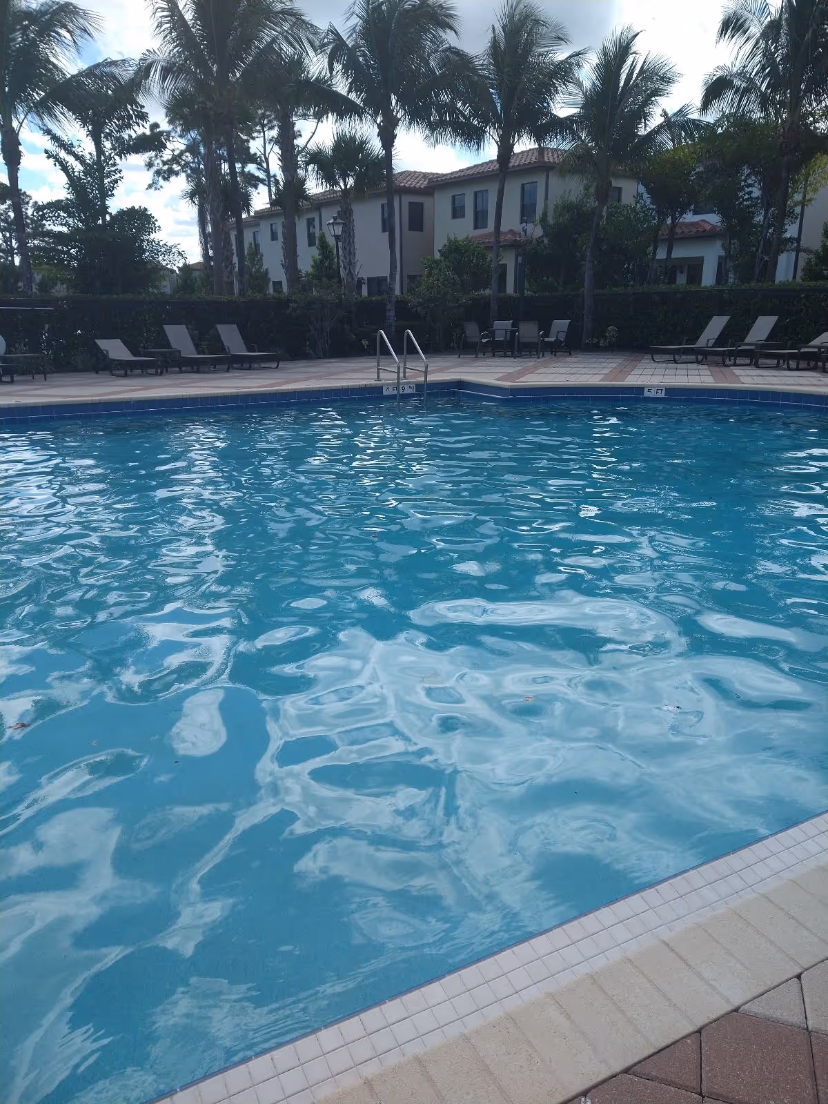 Outdoor pool area at True Angel Care Services with lounge chairs and palm trees.