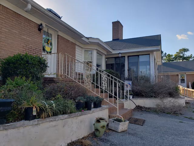 Front exterior of a single-story brick senior living facility with steps and potted plants.