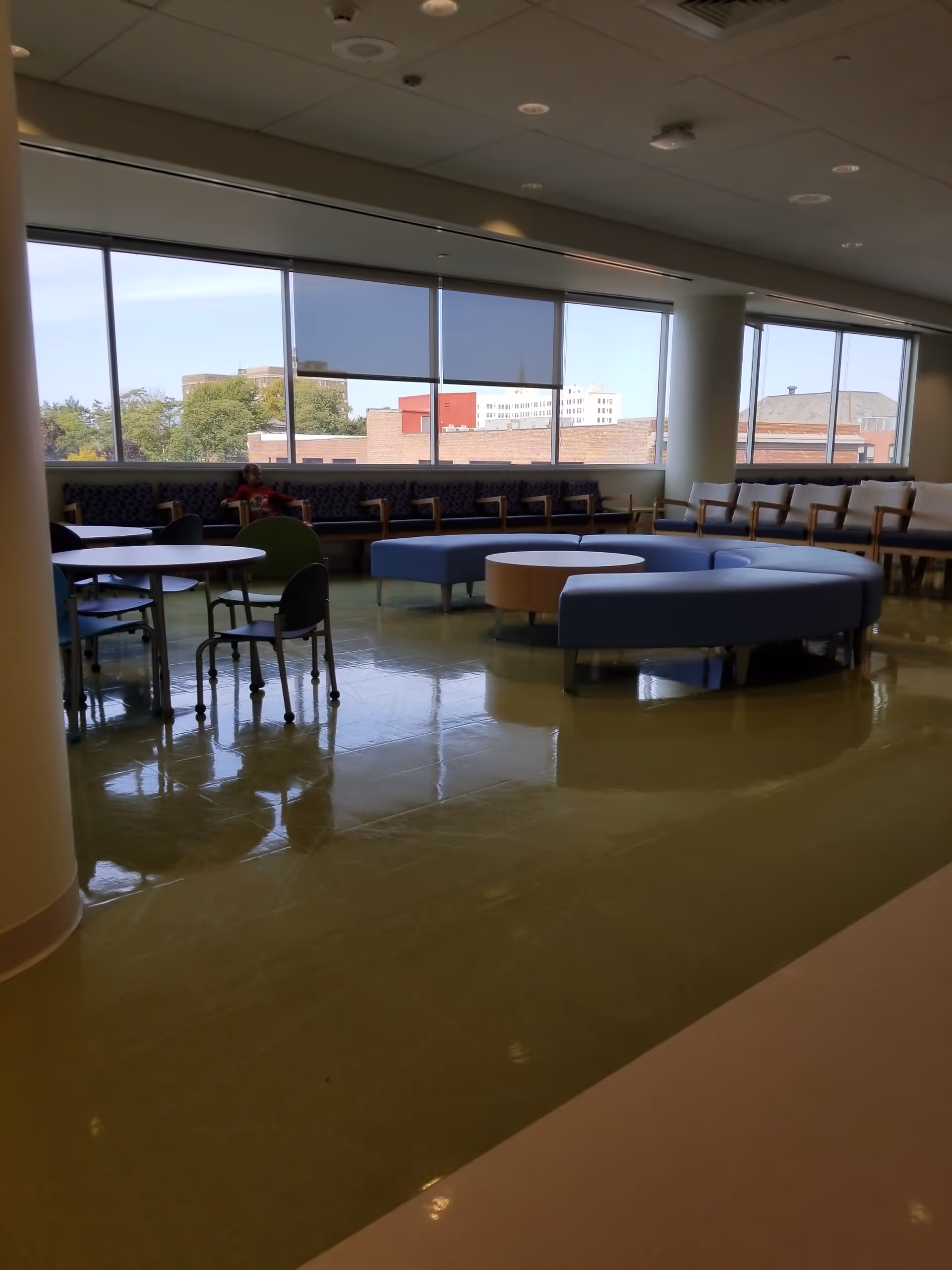Interior waiting area with curved blue seating, tables, and large windows.