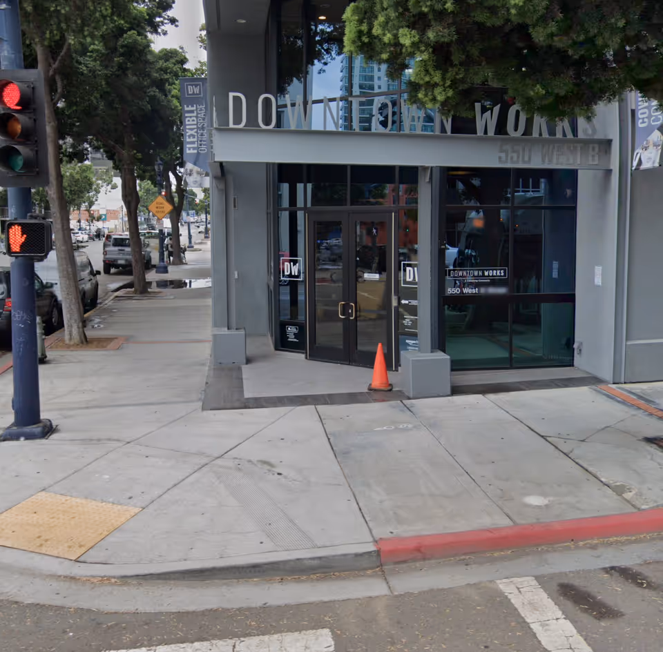 Urban storefront entrance with glass doors, Downtown Works signage, and a traffic cone.