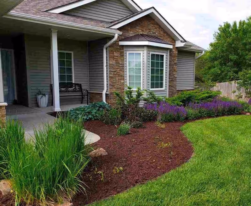 Front exterior of a residential building with porch, landscaped garden beds, and a green lawn.