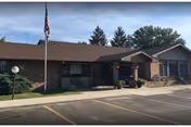 Single-story brick senior living facility with entrance, flagpole, and parking lot.