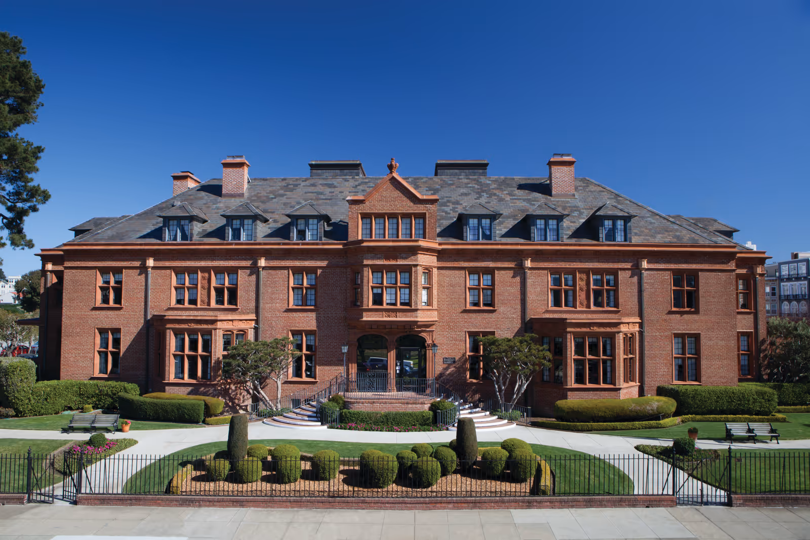 Red brick building with manicured lawns and a grand entrance under a clear blue sky.