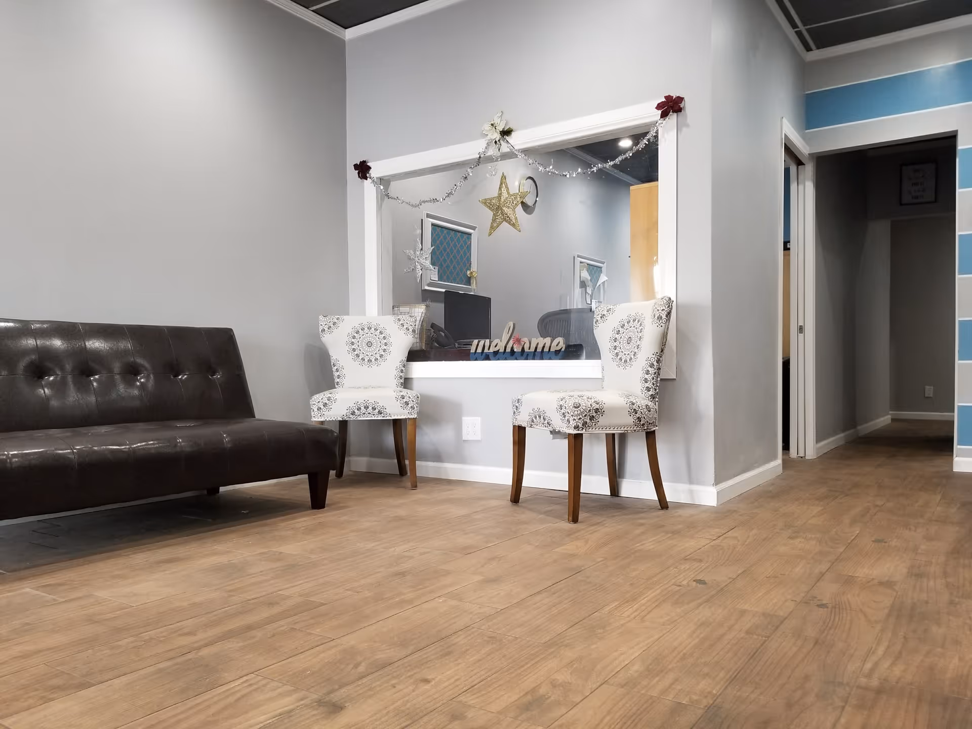 A modern lounge/reception area with a brown sofa, patterned chairs, and holiday garland.