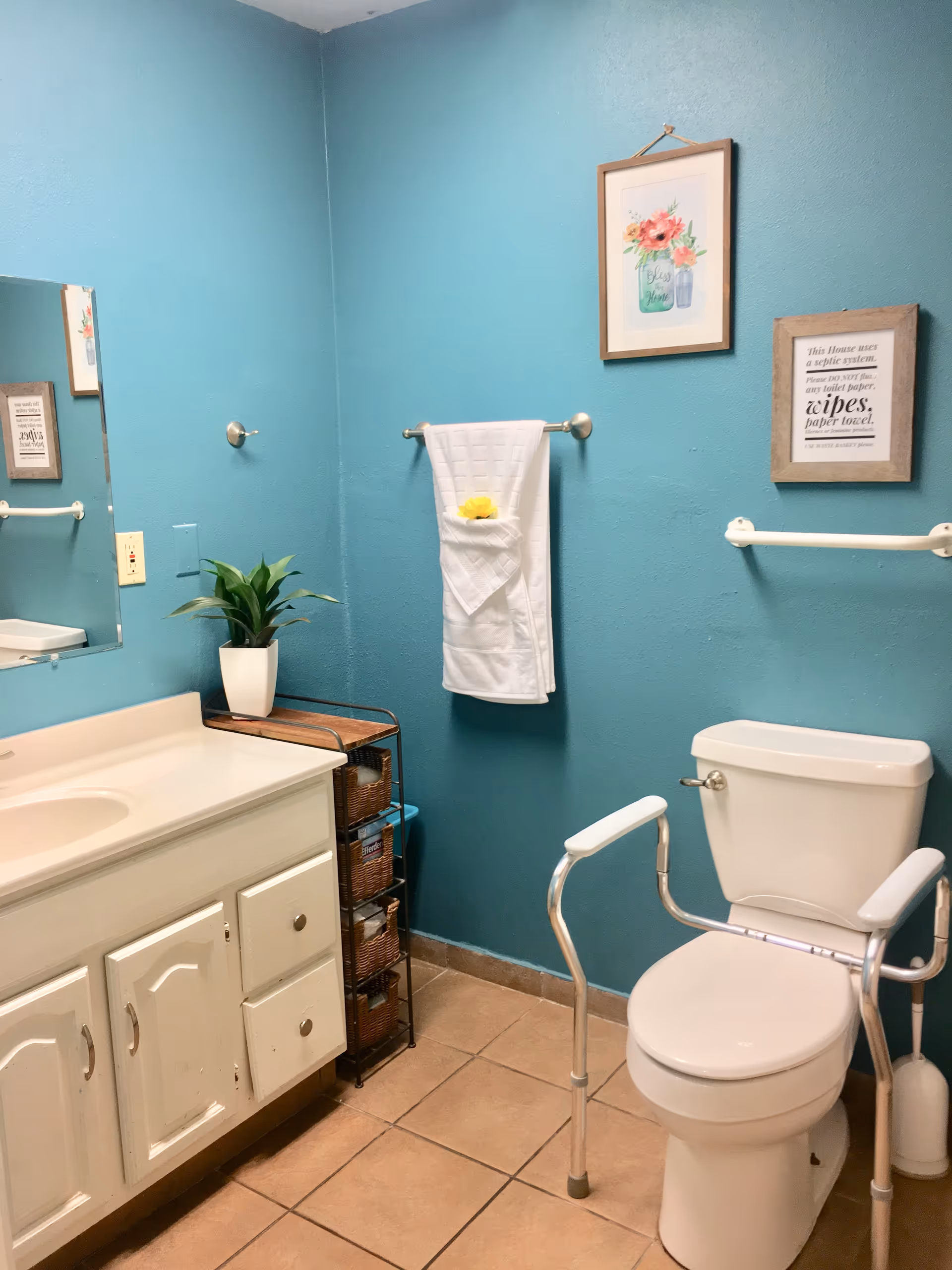 Teal bathroom with sink, mirror, toilet, towel rack, and wall art.