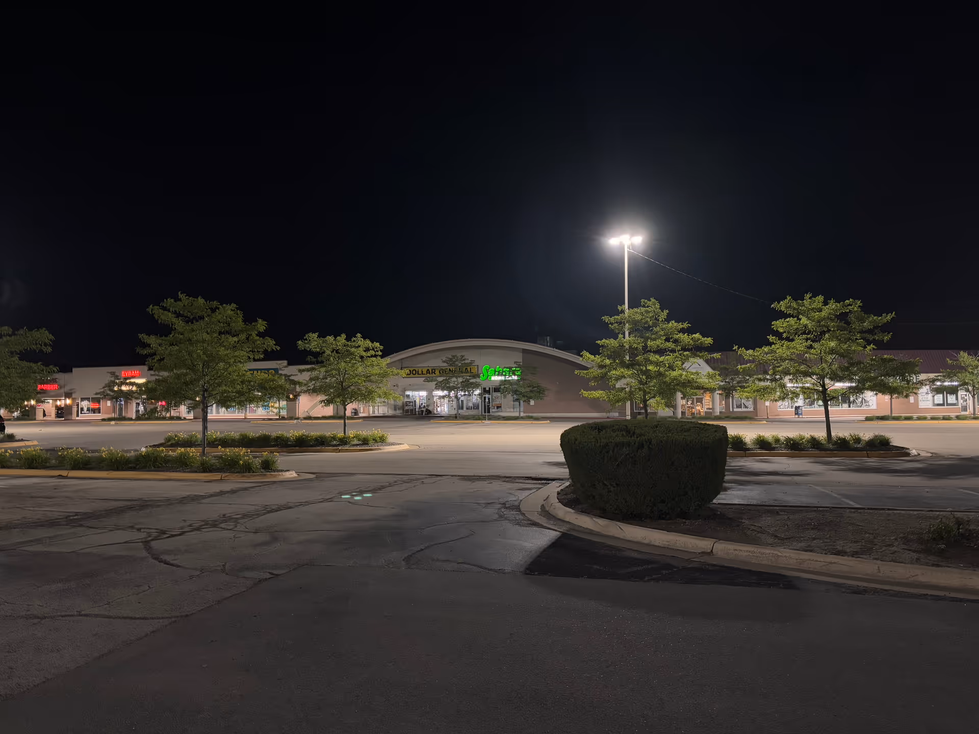 Nighttime exterior of a strip mall with storefronts and parking lot lighting.