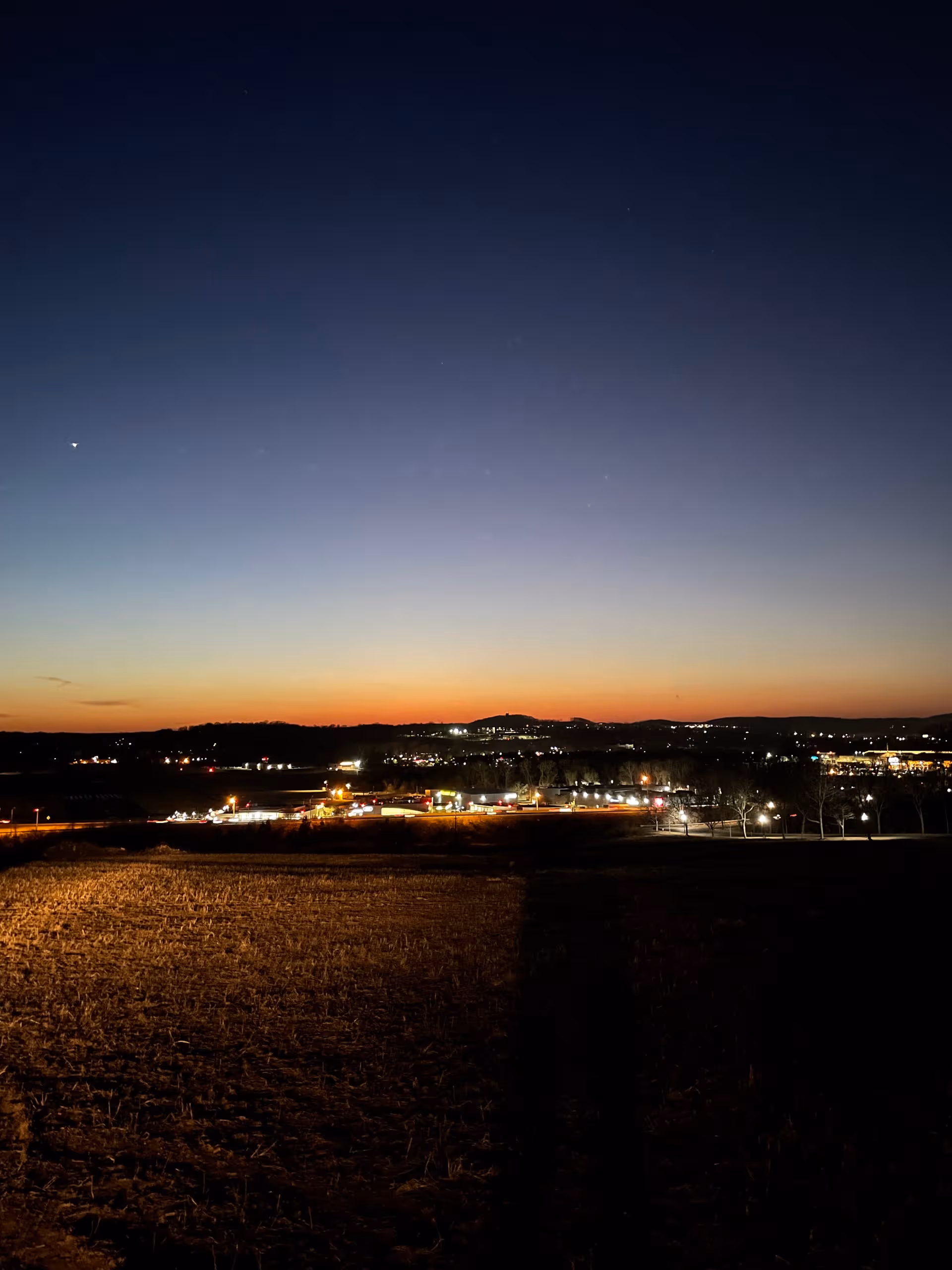 Nighttime landscape showing a grassy foreground and distant city lights along the horizon.