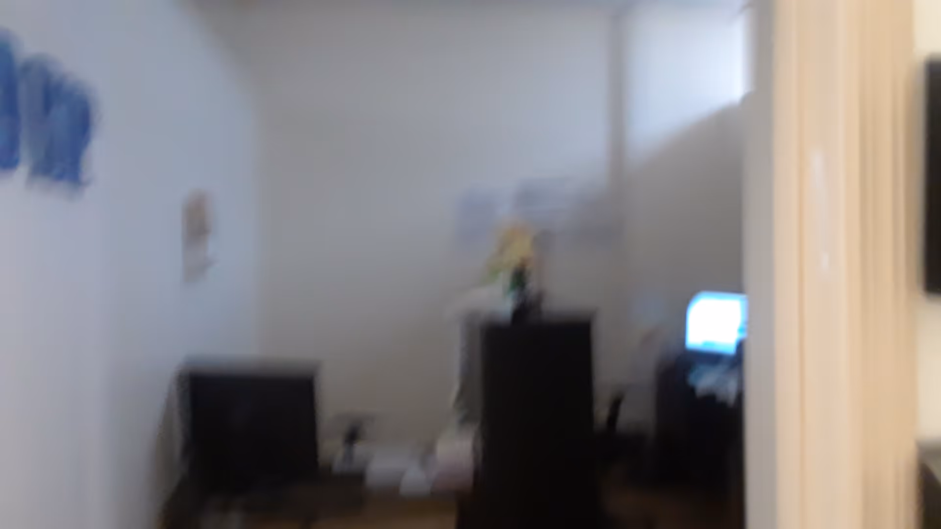 Blurry interior room with computer monitors, a tall cabinet, and a vase on top.