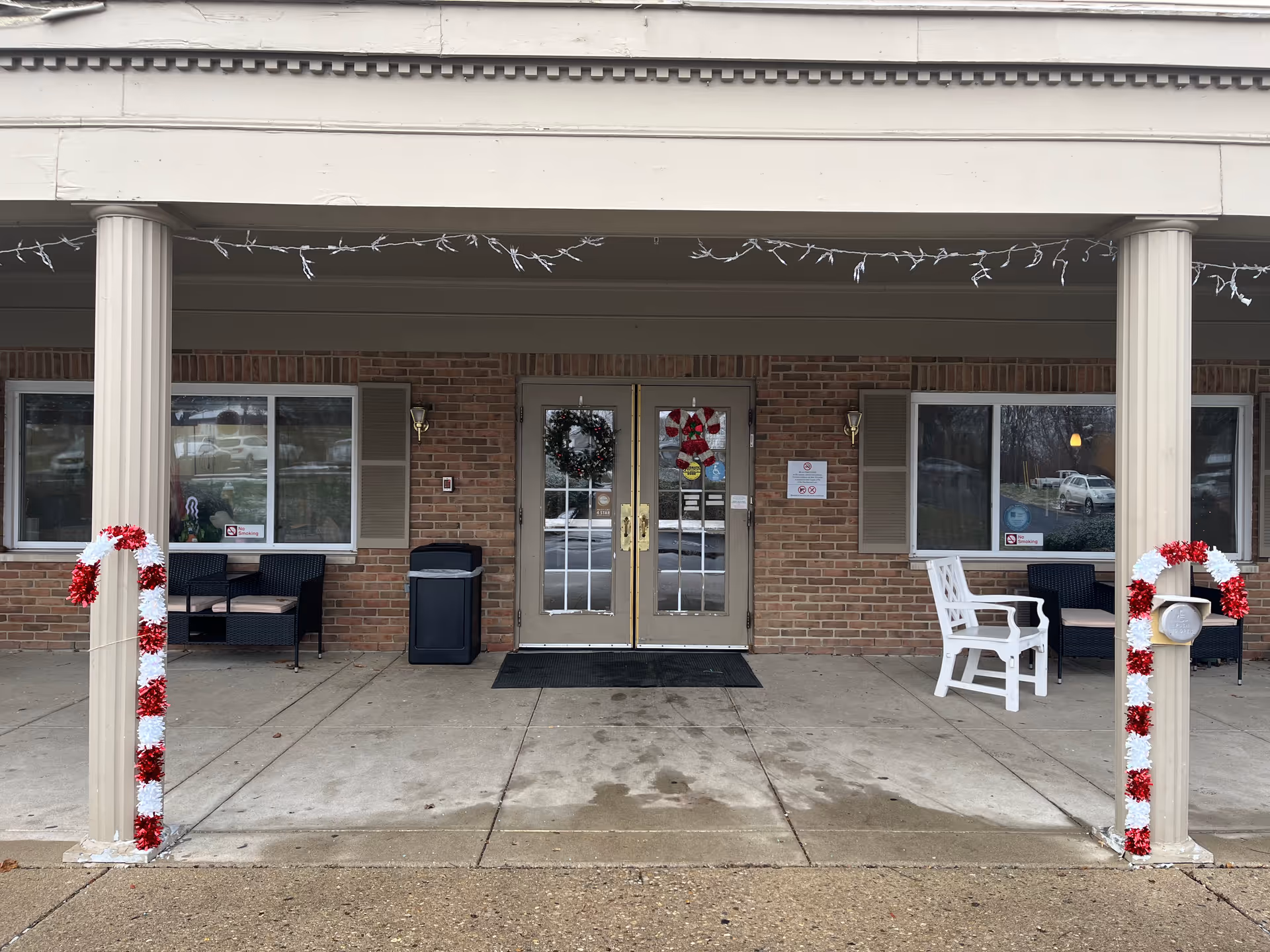 Brick building entrance to a senior living facility with wreaths, chairs, and a covered porch.