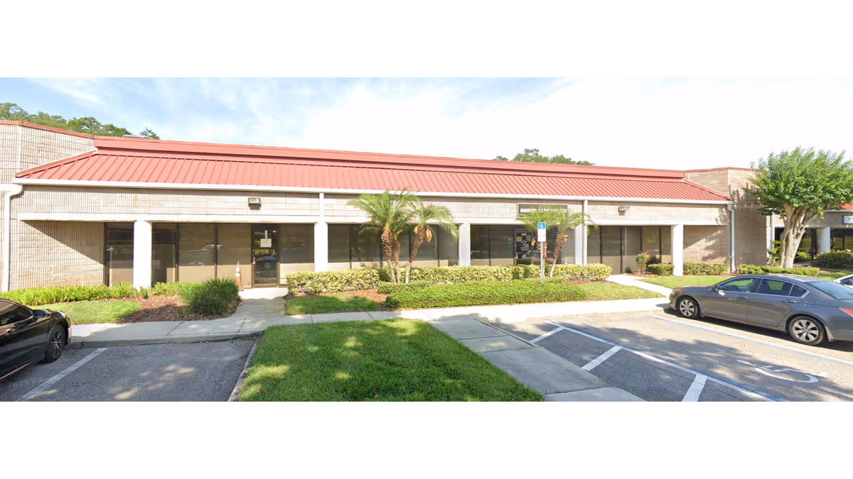 Exterior view of Soleo Health facility with red roof, glass doors, and parking.