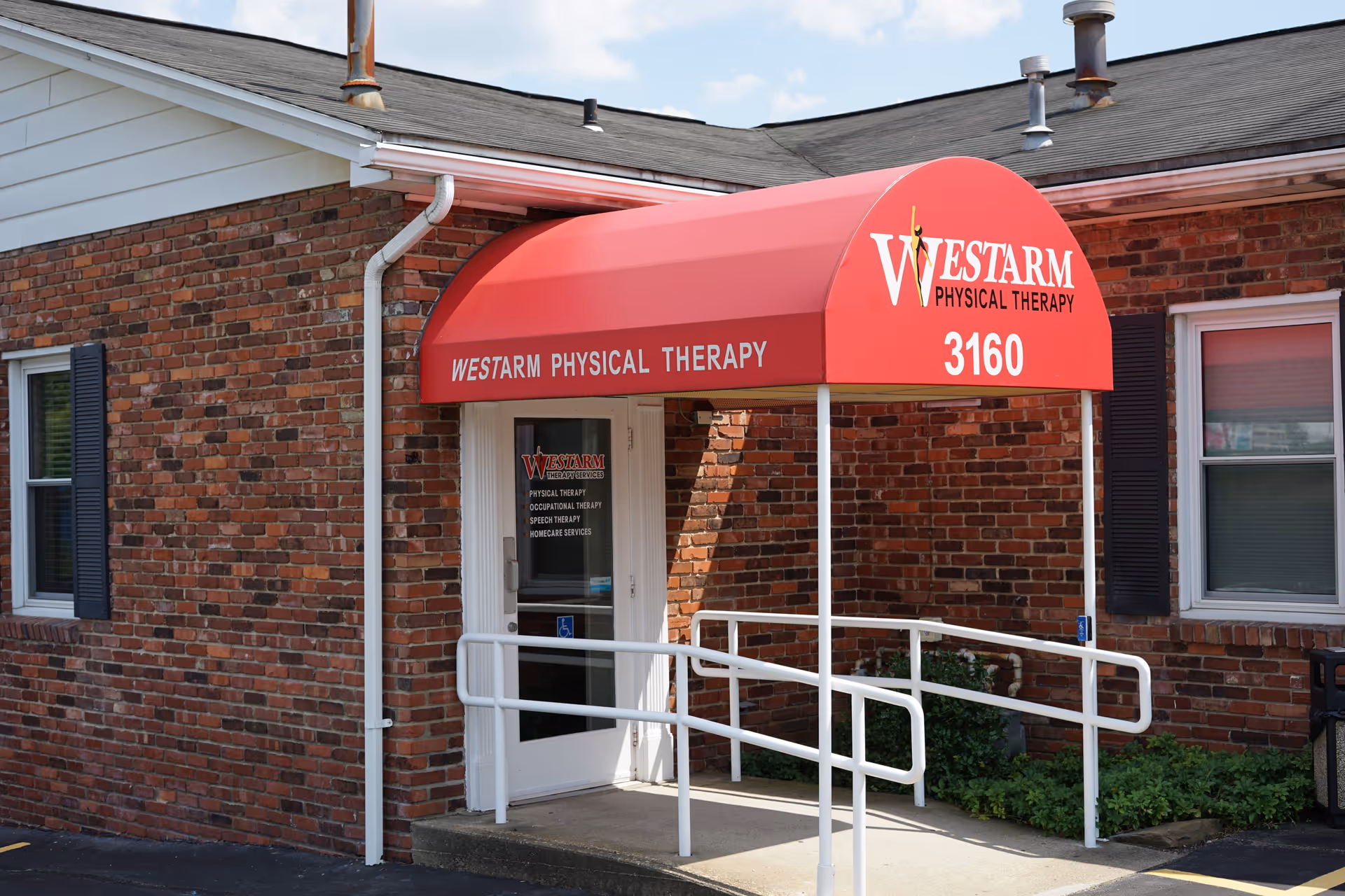 Brick building exterior with a red curved awning reading Westarm Physical Therapy and entrance ramp.