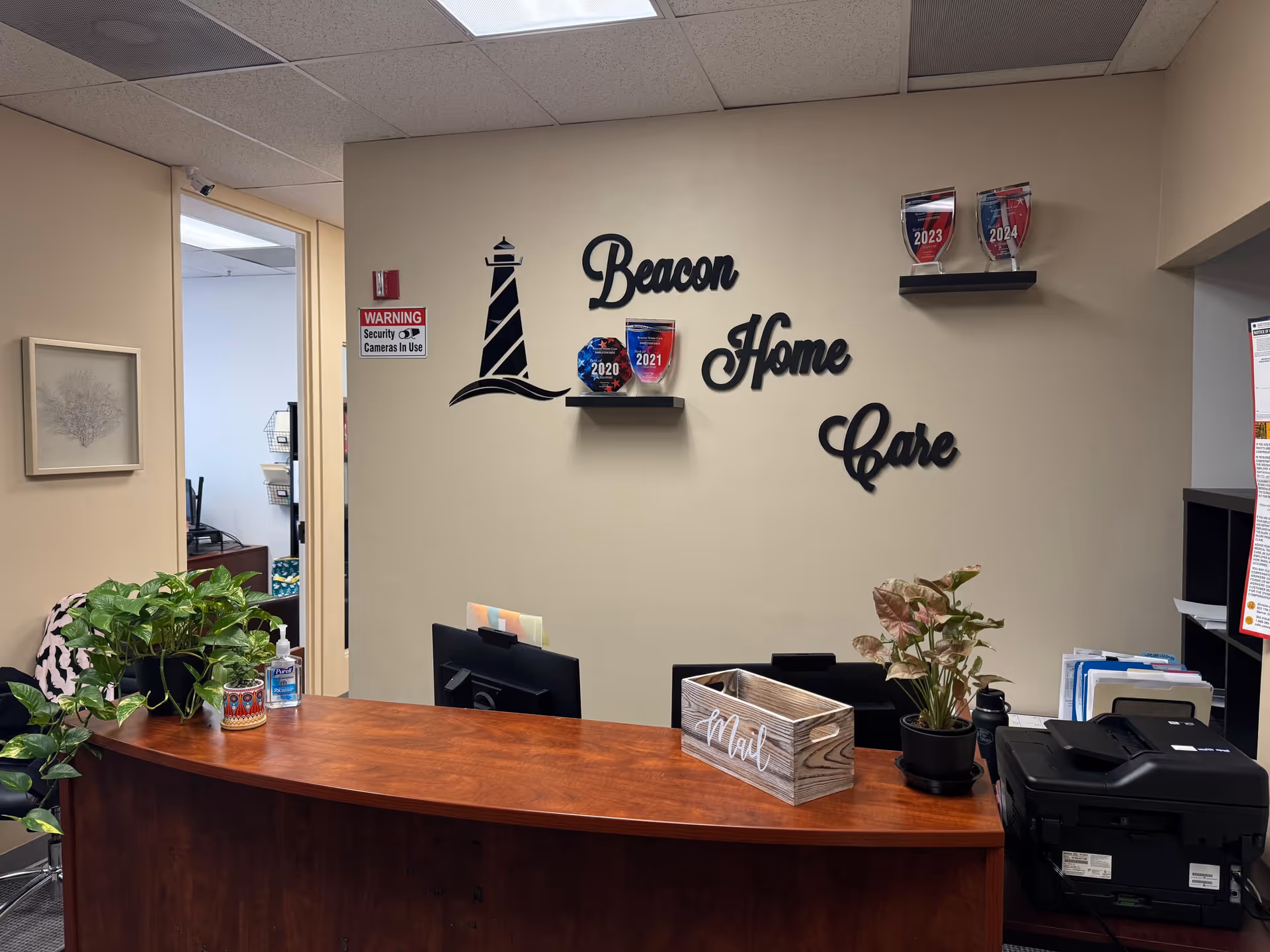 Reception desk in Beacon Homecare lobby with plants, wall sign, and office doorway.