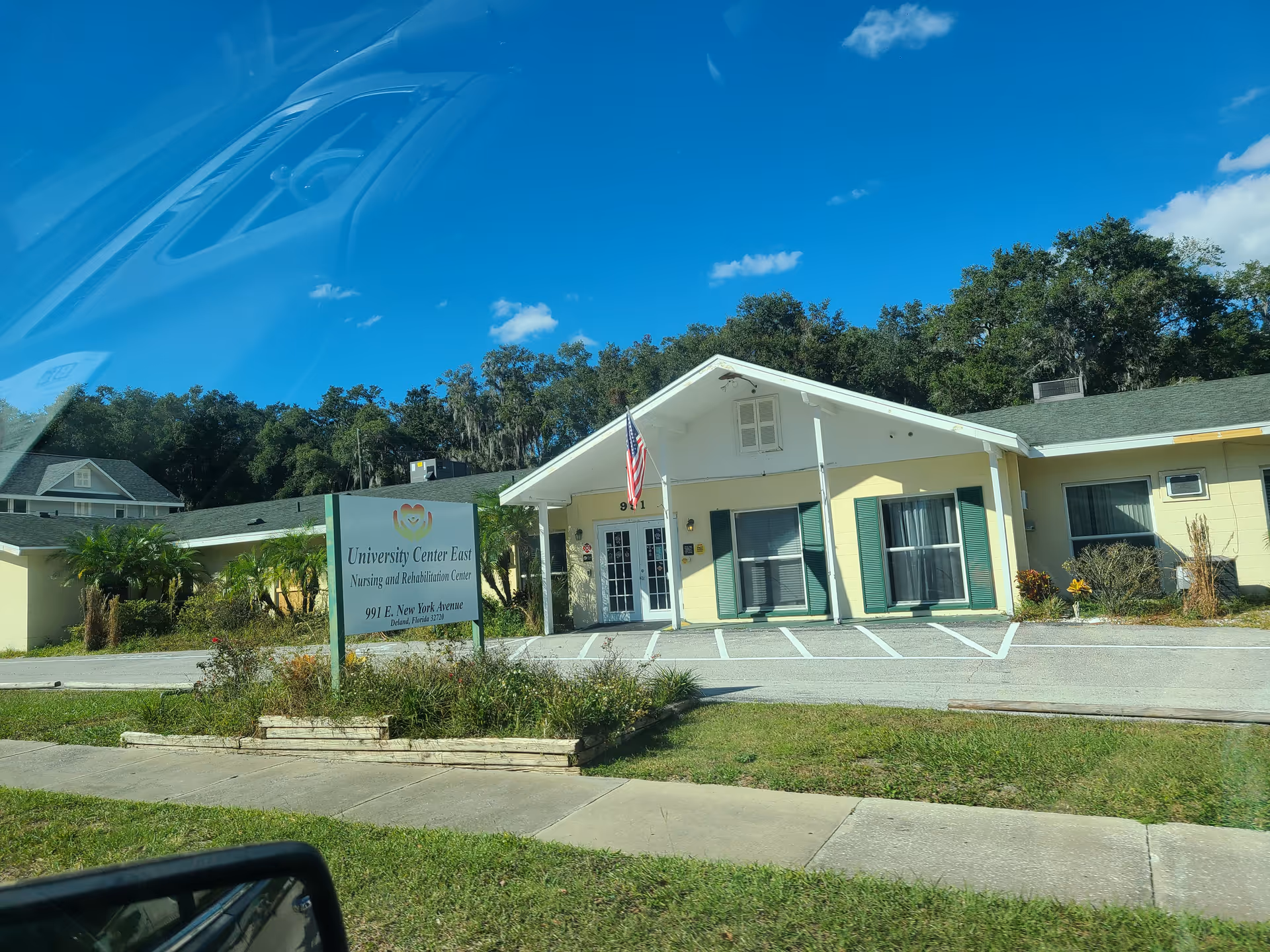 Single-story nursing center exterior with front entrance, flag, and sign visible in landscaping.