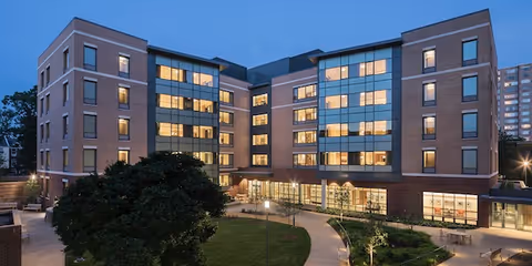 Exterior view of a brick senior living facility at dusk with lit windows.