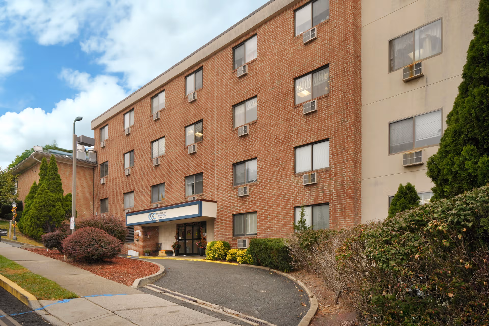 Brick senior living residence exterior with entrance canopy and landscaped surroundings.
