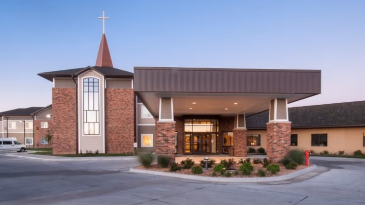 Exterior view of a brick senior living facility with a prominent covered entrance and cross.