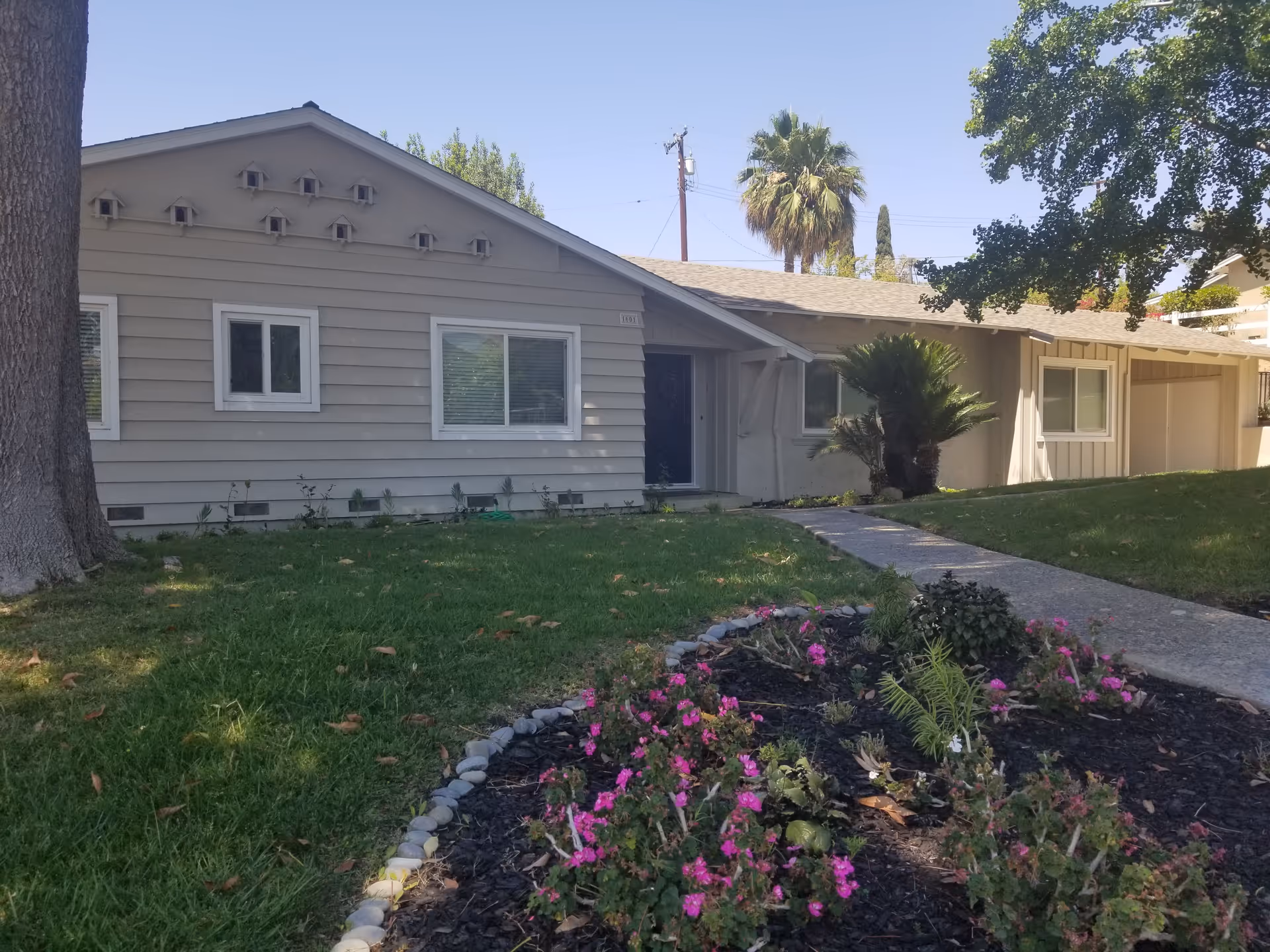 Front exterior of a single-story house with a lawn, walkway, and a flowerbed in the foreground.