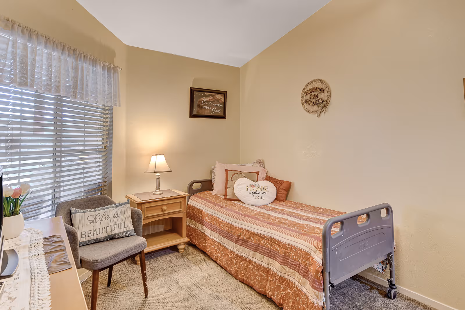 Cozy beige bedroom with single bed, chair, nightstand, and window blinds.