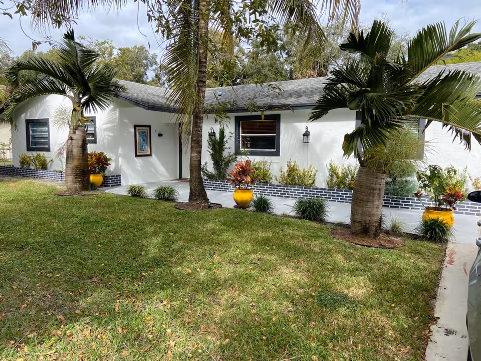 White, single-story facility exterior with palm trees, shrubs, and yellow planters.