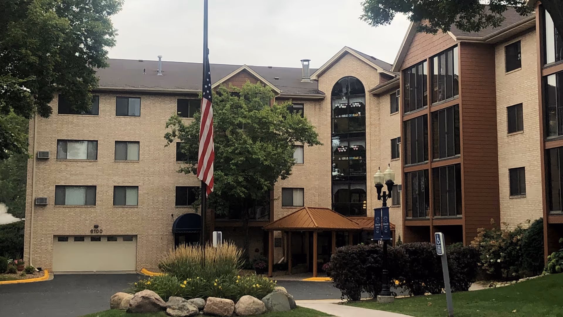 Exterior view of a senior living facility with flagpole, glass entrance, and landscaping.