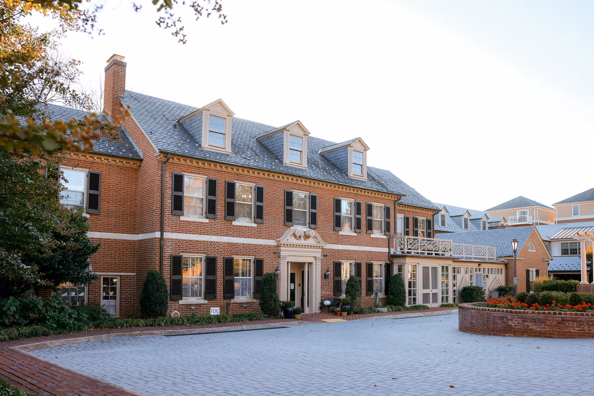 Front exterior of a large brick senior living facility with a paved driveway and landscaped flowerbeds.