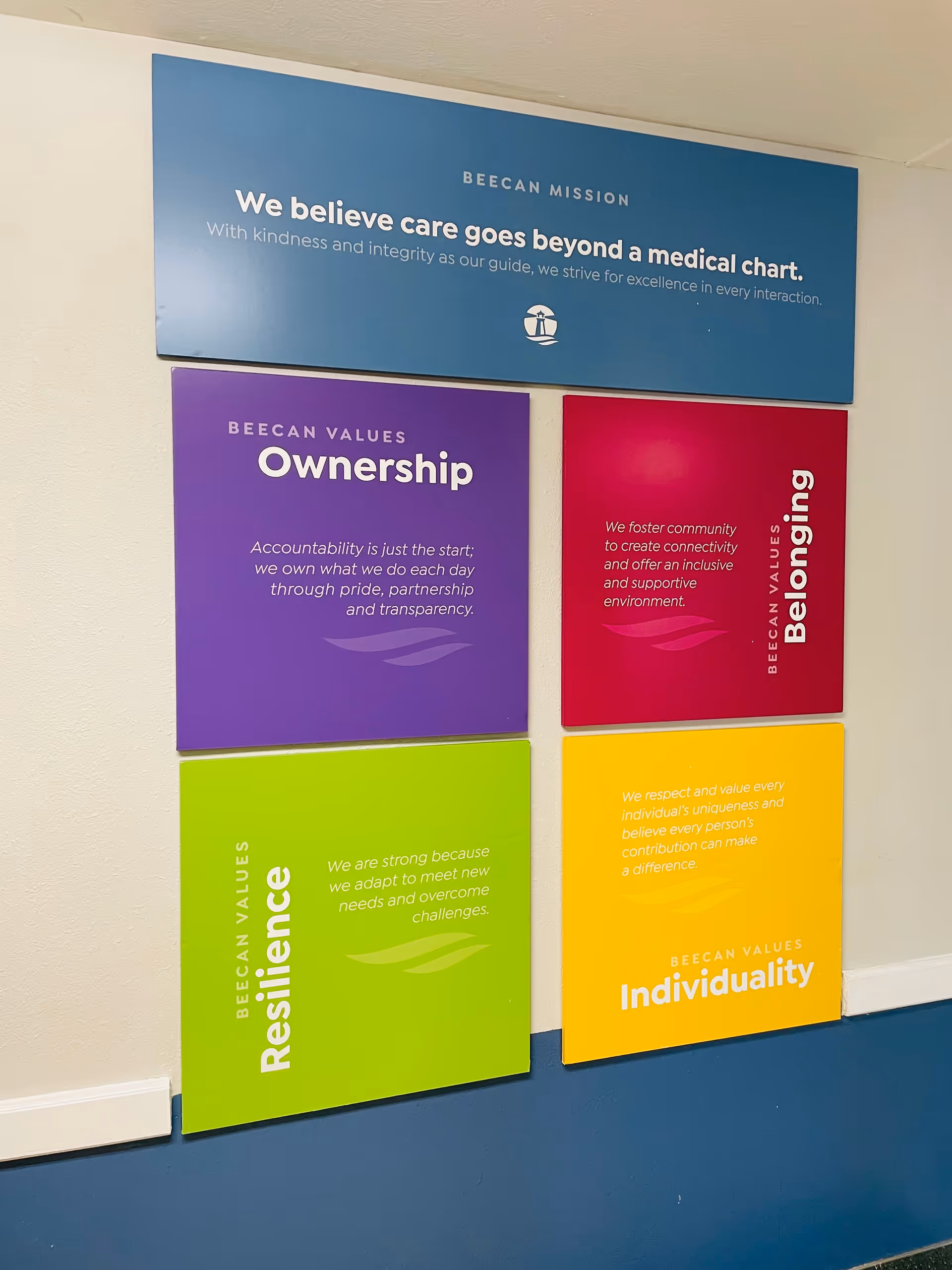 Six colorful Beecan values posters on a blue and beige hallway wall.