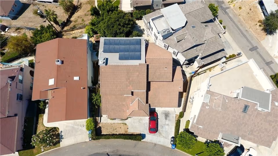 Aerial view of multiple residential homes with brown and gray rooftops along a curved street.