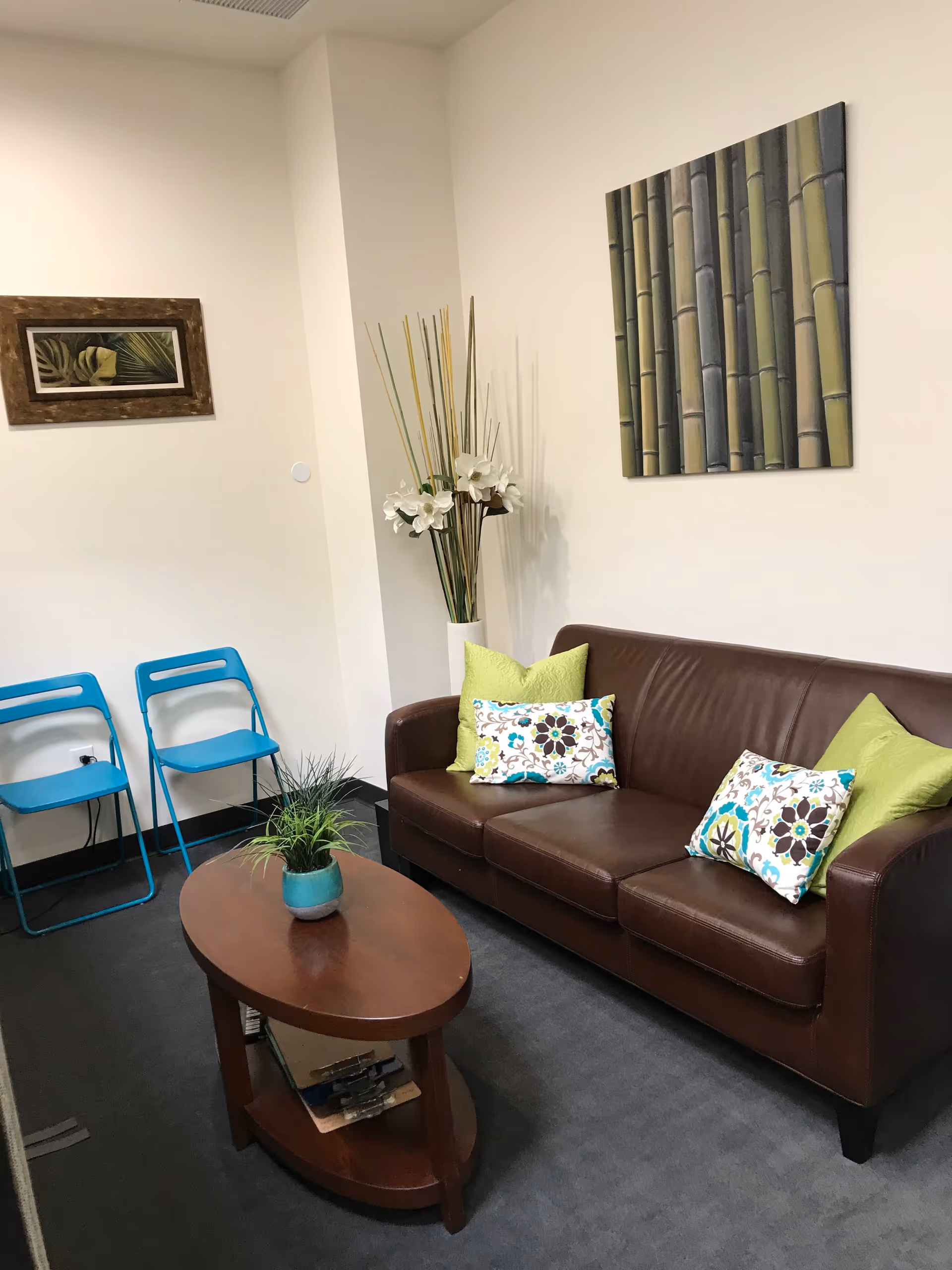Cozy senior living facility lounge with brown sofa, blue chairs, and decorative plants.