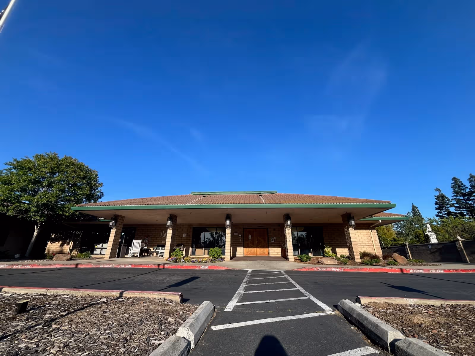 Brick-built senior living facility with a covered entrance and parking lot under a clear blue sky.
