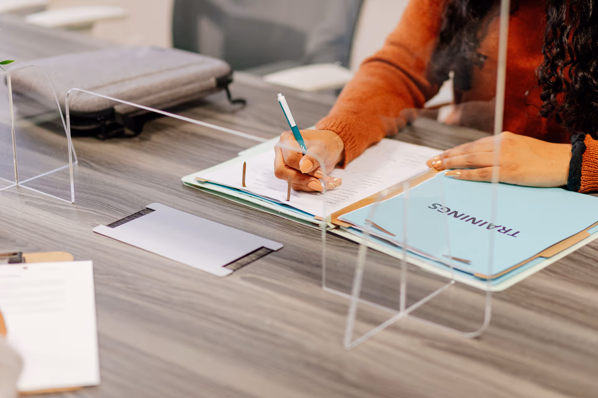 Hands sign documents at a desk with folders and clear acrylic dividers.