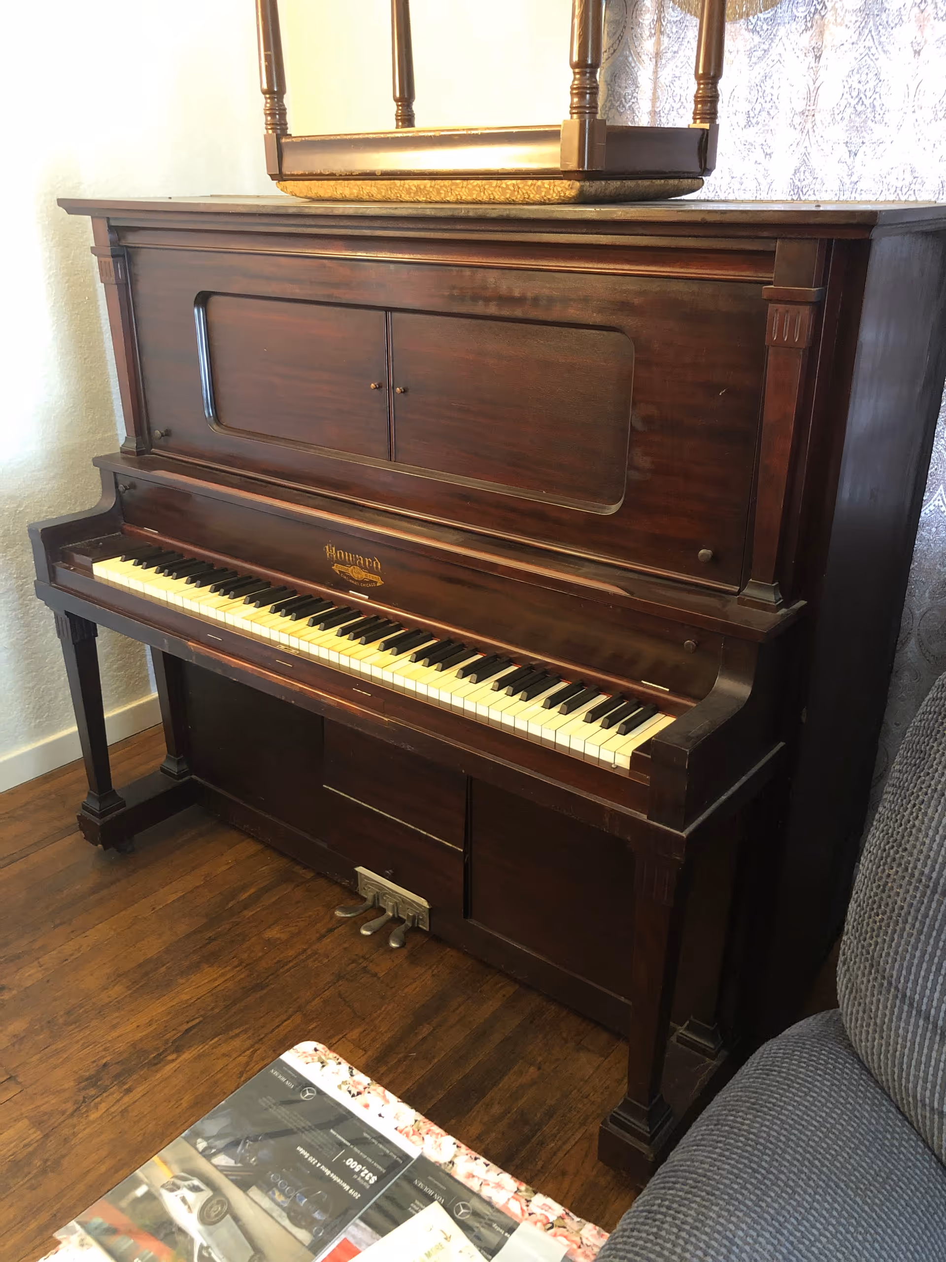 Dark wooden upright piano in a cozy living room, with a sofa and magazines