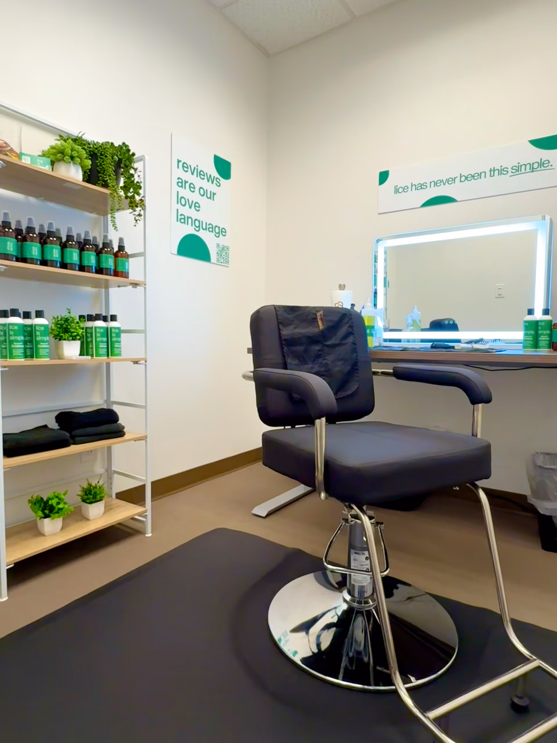 A modern salon chair sits in a well lit treatment room with shelves and a mirror.