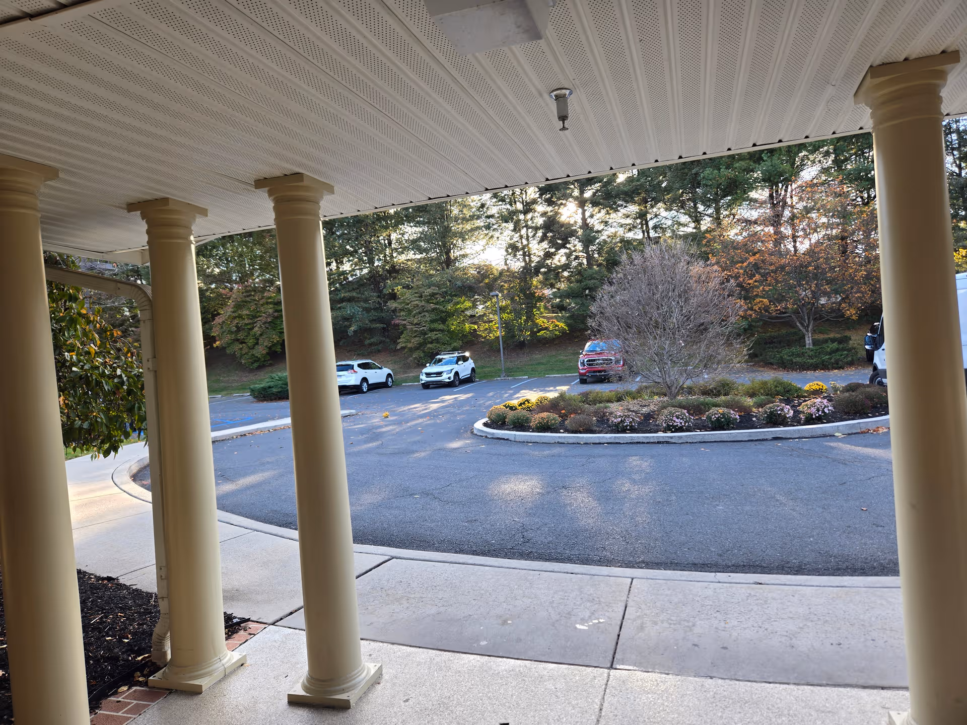 Covered walkway with cream columns overlooking a circular driveway and landscaped center at Brookdale Grandon Farms.