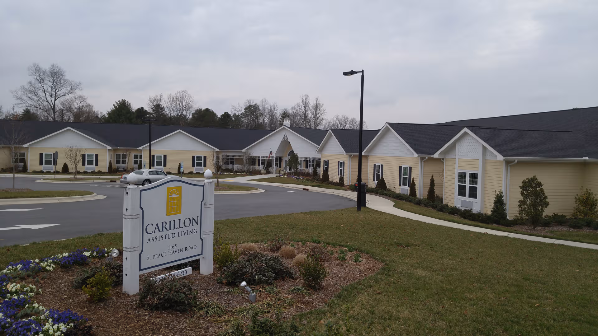 Exterior view of Carillon Assisted Living facility with curved driveway and landscaped sign garden.